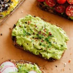 Four vibrant avocado toast recipe creations, artfully arranged on a wooden board with various fresh toppings.